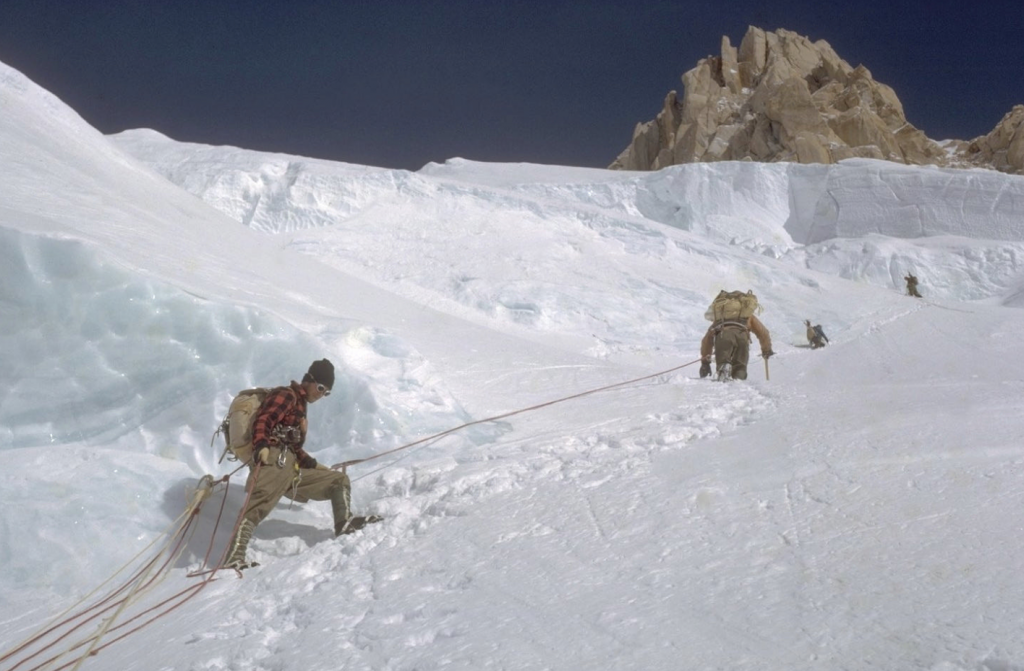 Three climbers on a steep snowfield with a rocky summit above them